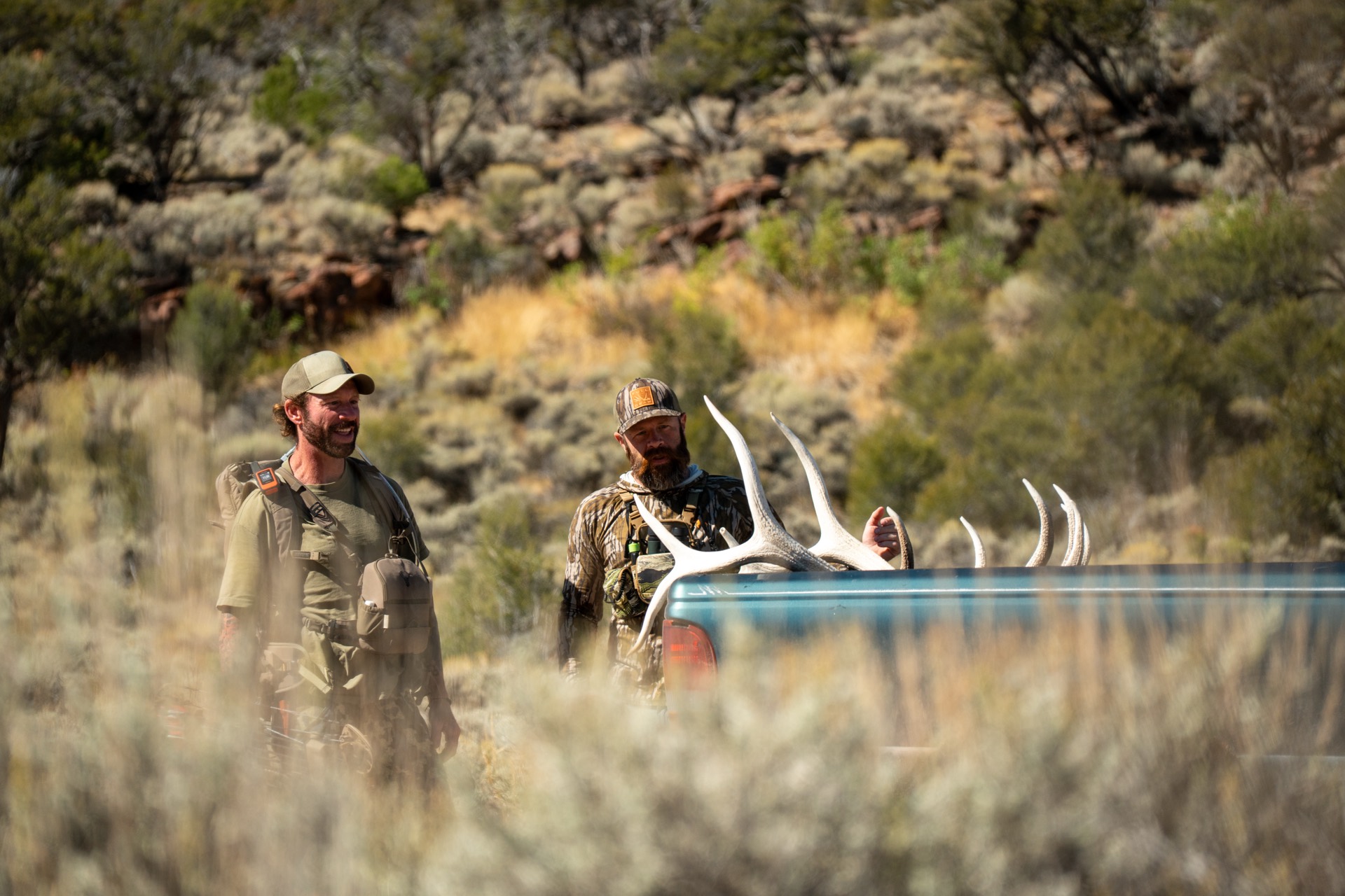 Two hunters loading elk antlers into a pickup in sage country