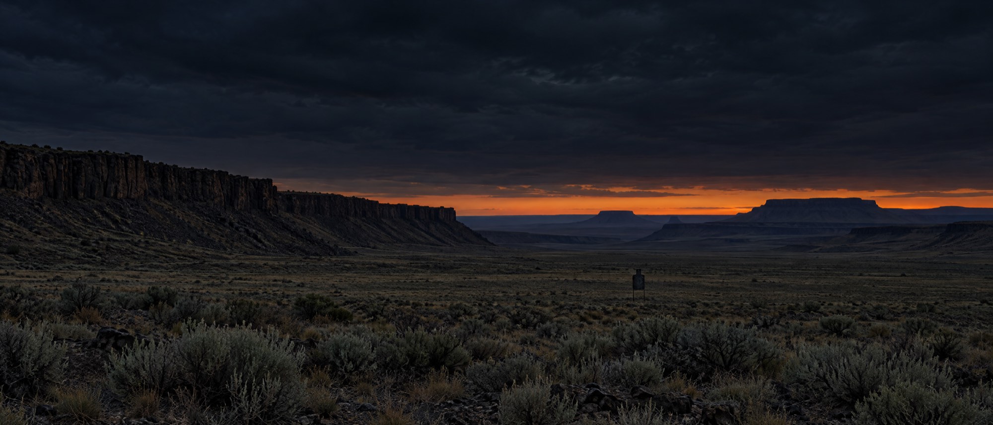 High-desert rimrock at dusk with a single steel target set out on the flat